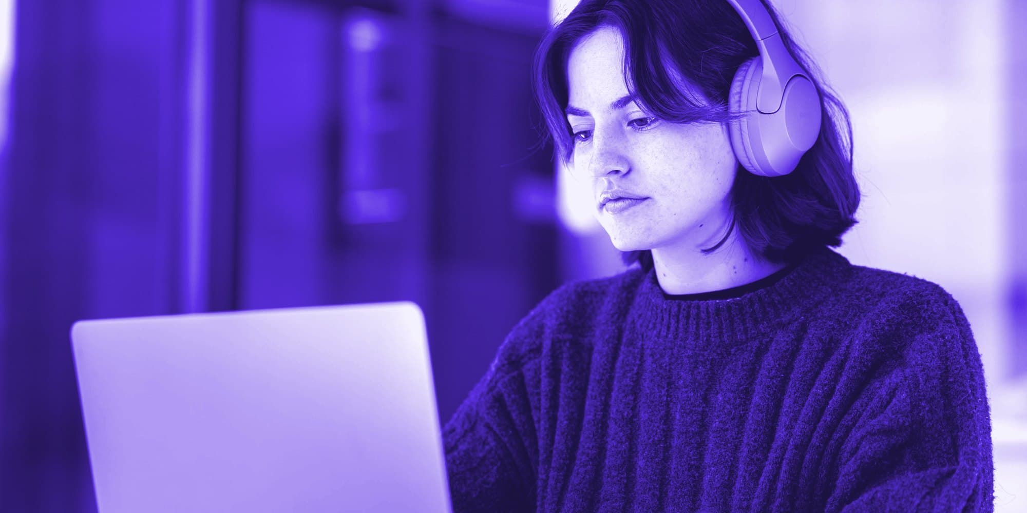 A woman in headphones, focused on her laptop