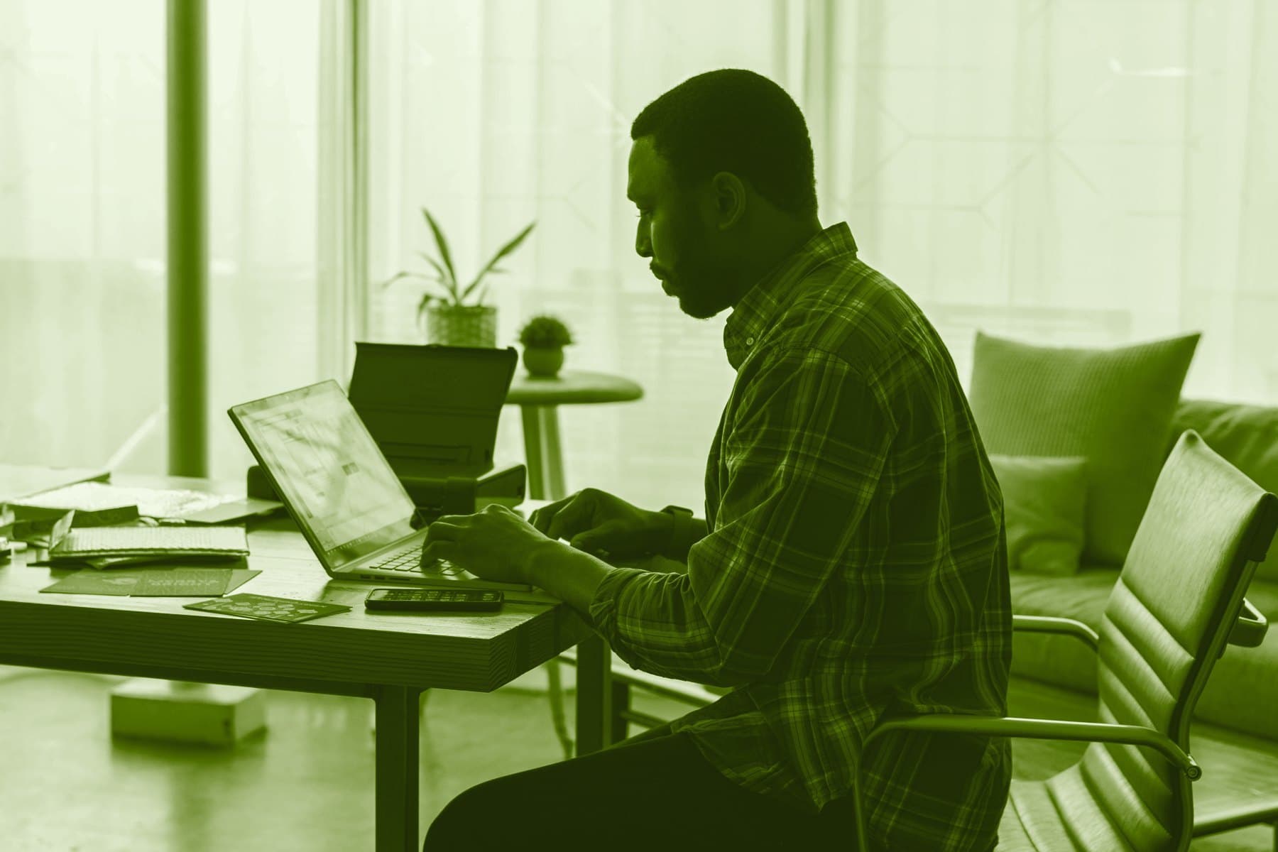 A man working on his own at a laptop, at a desk by a bright window