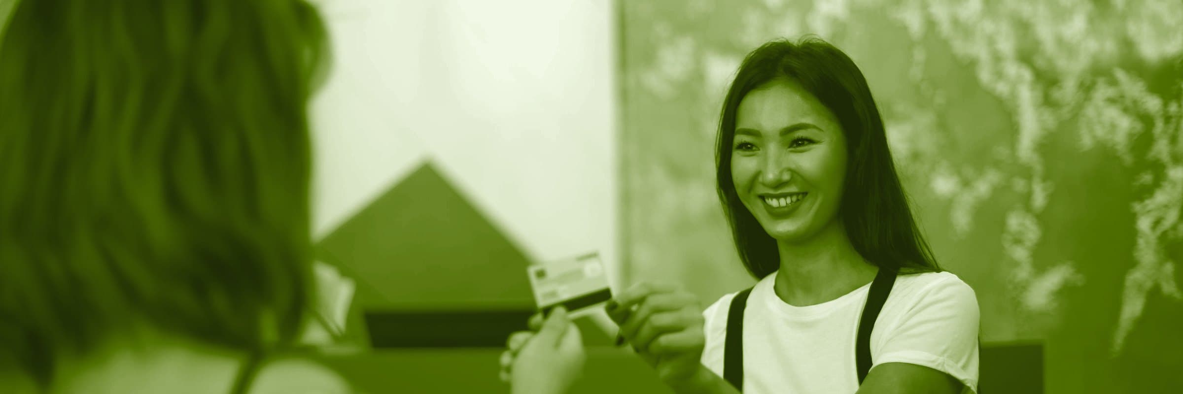 A smiling shopkeeper in an apron taking a customer's card at the counter