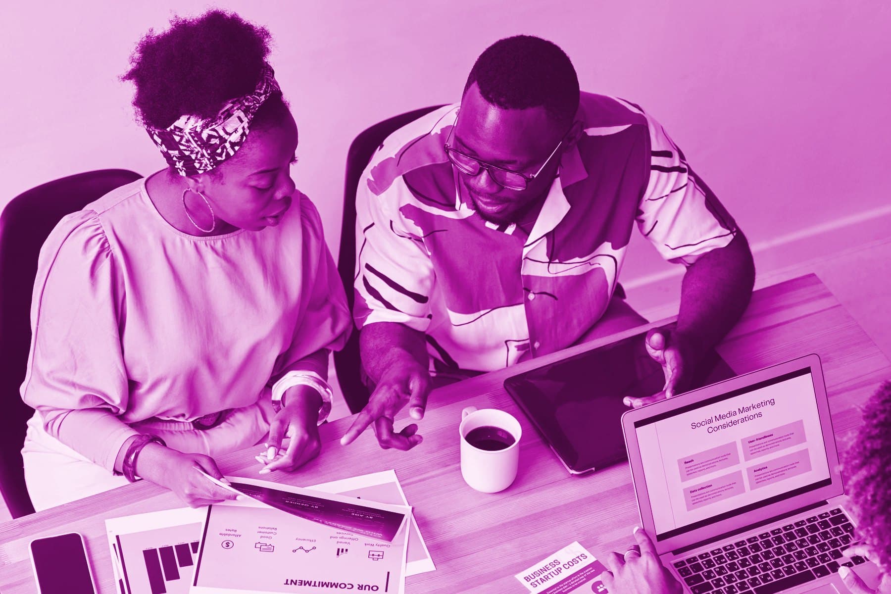 Two colleagues at a table going through printed pages beside a laptop